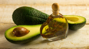 Bottle of avocado essential oil with fresh avocado fruit closeup
